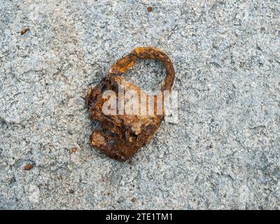 Un vecchio lucchetto arrugginito che si trova sul fondo del fiume da molti anni su una pietra di granito piatta. Contesto Foto Stock