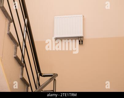 Radiatore di riscaldamento montato in alto sulla parete nel corridoio d'ingresso sul pianerottolo di un edificio moderno Foto Stock