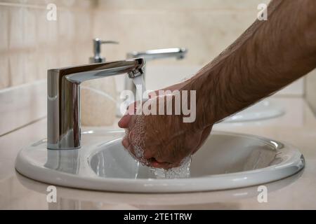 Le mani di un uomo che si lava le mani sotto l'acqua corrente da un rubinetto Foto Stock