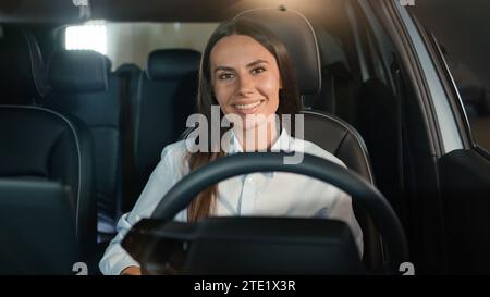 Felice gioiosa toothy sorridente donna caucasica sorridente guardando la macchina fotografica sedersi all'interno di una nuova auto di lusso a noleggio, una ragazza autista femminile alla guida di un'automobile Foto Stock