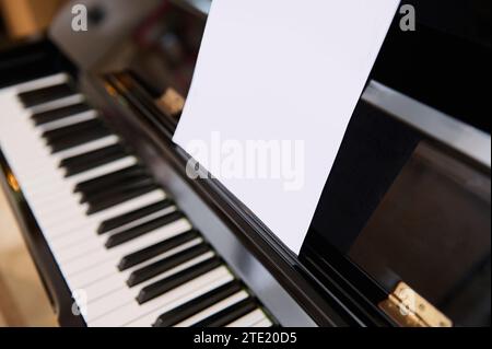 Primo piano del pianoforte classico e foglio di carta bianca con note musicali per eseguire la composizione musicale. Imparare la musica e suonare sul luxu classico Foto Stock