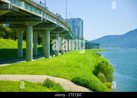 Namyangju City, Corea del Sud - 30 settembre 2023: Percorsi ciclistici e pedonali si snodano sotto le torreggianti colonne di Gyeonggang Road, con il fiume Han Foto Stock