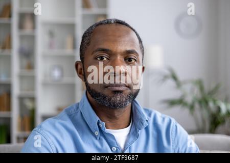 Ritratto ravvicinato di un uomo afro-americano seduto a casa, guardando con serietà e sicurezza la fotocamera. Foto Stock