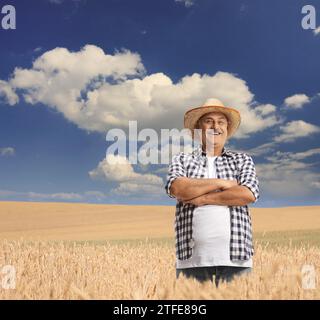 Agricoltore maturo in un campo di grano che posa in una giornata di sole con cielo blu e nuvole bianche Foto Stock