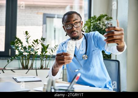medico afro-americano pensivo consultando il paziente per telefono e tenendo pillole, telemedicina Foto Stock