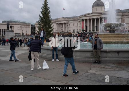 I turisti festivi si fanno dei selfie e delle foto l'uno dell'altro di fronte alle fontane di Trafalgar Square nel West End di Londra, 20 dicembre 2023 Foto Stock