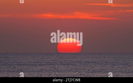 Il sole che tramonta. Un disco rosso/arancione nel cielo. Foto Stock