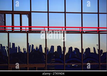 Un riflesso dello skyline di New York appare nelle finestre di vetro di un moderno edificio Office con una ringhiera rossa intorno ad un balcone Foto Stock