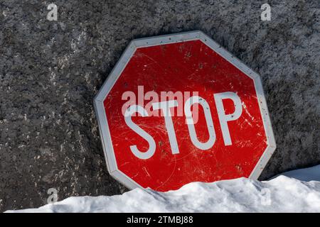 Fermata , segnaletica stradale su sfondo cemento. Terreno coperto di neve. Colori rosso e bianco. Informazioni. Foto Stock