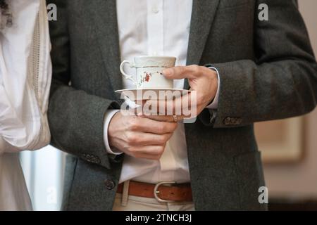 Uno sposo appena sposato tiene una bella tazza da tè con la sua fede nuziale mentre ascolta i discorsi Foto Stock