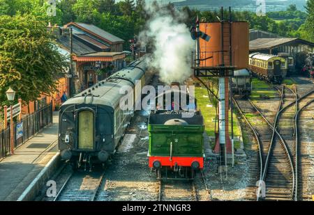 Stazione ferroviaria di Buckfastleigh, Devon, con un motore che soffia vapore e passeggeri che aspettano sulla piattaforma della stazione. Foto Stock