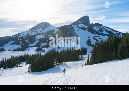 Attraversando il sentiero innevato Panorama Ridge Trail, un escursionista si avvicina alla suggestiva silhouette della Black Tusk Mountain nel famoso Garibaldi Pro della British Columbia Foto Stock