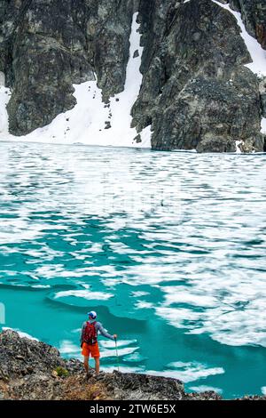 Un escursionista rifrangente si ferma sulle rive ghiacciate del lago Wedgemount, immerso nella grandiosità delle Montagne Rocciose canadesi. Foto Stock