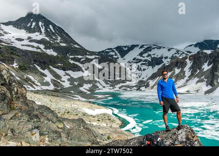 Un avventuriero in posa si trova vicino al vivace lago Wedgemount, pronto per la salita. Foto Stock