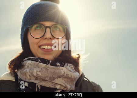 Il bagliore del sole aggiunge una qualità da sogno al sorriso beato della donna, avvolto in stile invernale Foto Stock