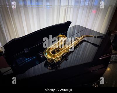 Un sassofono color oro giace su un pianoforte a coda da concerto nero Foto Stock
