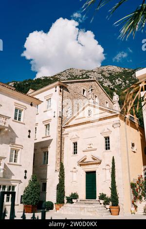 Chiesa di S.. Segnate l'Apostolo tra antiche case e alberi verdi in vasi di fiori. Perast, Montenegro Foto Stock