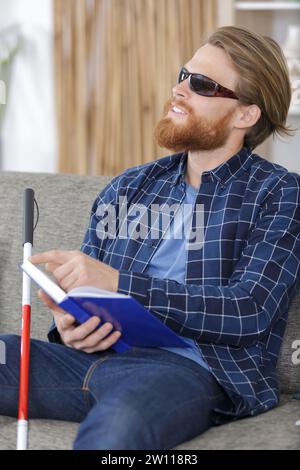 un uomo cieco che legge un libro scritto in braille sul divano Foto Stock