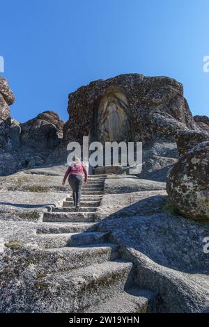 Donna escursionista sul sentiero con scale per la scultura di Santa Maria Senhora da Boa Estrela scolpita nella roccia di granito, Serra da Estrela, Portogallo Foto Stock