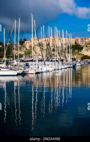 Barche a vela all'ancora nel porto e nel porticciolo di Tropea, le case della città su una scogliera in lontananza. Foto Stock