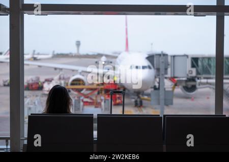 Donna seduta sulla schiena, guarda dalla finestra dell'aeroporto, aspettando il suo volo. Foto Stock