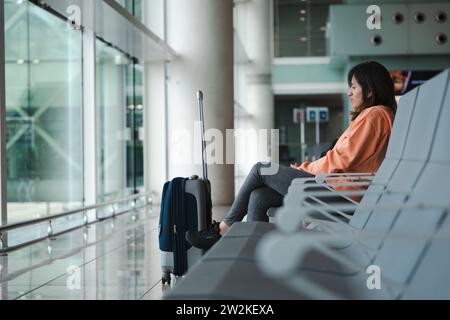 Donna seduta, guarda dalla finestra dell'aeroporto, aspettando il suo volo. Foto Stock