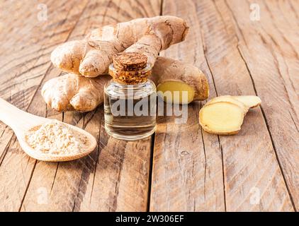 Olio essenziale di radice di zenzero in bottiglia di vetro con tappo in sughero su un tavolo di legno con radice . Ringiovanimento della pelle, rafforzamento della crescita dei peli Foto Stock