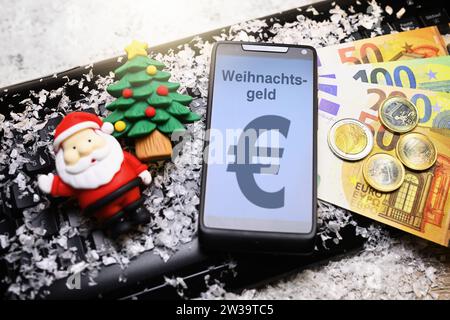 FOTOMONTAGE, smartphone mit Aufschrift Weihnachtsgeld, Geldscheine, Weihnachtsmannfigur und Tannenbaum auf Computertastatur Foto Stock