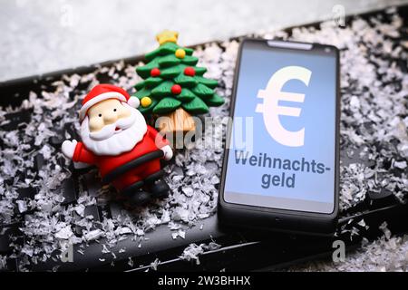 FOTOMONTAGE, smartphone mit Aufschrift Weihnachtsgeld, Weihnachtsmannfigur und Tannenbaum auf Computertastatur Foto Stock