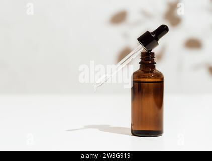 Bicchiere marrone con contagocce e una goccia d'essenza. Contagocce per olio cosmetico per flacone su una pipetta di vetro. Copia spazio Foto Stock