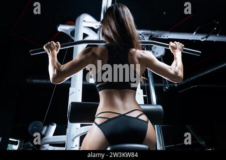 Una deliziosa sportiva esegue l'esercizio. Trazione dell'asse. Esercizio per i muscoli della schiena. Il concetto di sport, bodybuilding, nutrizione sportiva. Misto Foto Stock