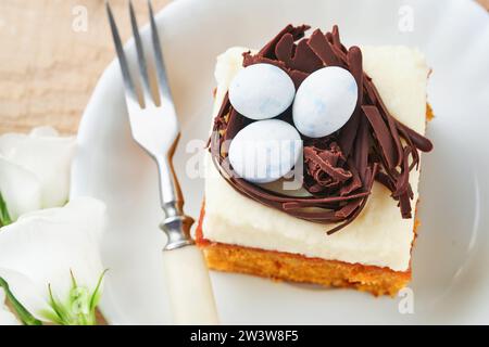 Barrette di carote pasquali decorate con nido di cioccolato e uova di caramelle al cioccolato fiorenti fiori di ciliegia o mela su sfondi rustici di legno chiaro. Foto Stock