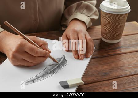 Donna che disegna piume con matita di grafite in un quaderno di bozzetti al tavolo di legno, primo piano Foto Stock