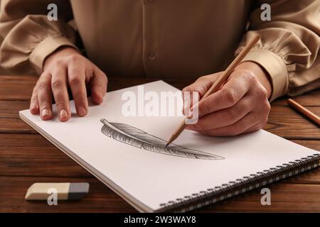 Donna che disegna piume con matita di grafite in un quaderno di bozzetti al tavolo di legno, primo piano Foto Stock