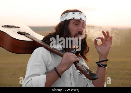 Elegante uomo hippie con fumante chitarra in campo Foto Stock