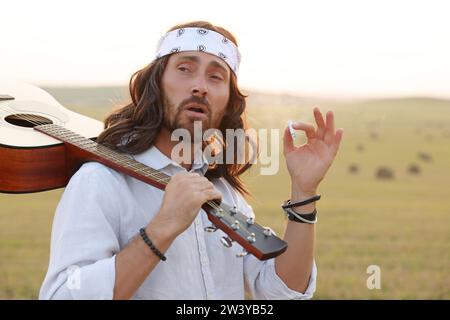 Elegante uomo hippie con fumante chitarra in campo Foto Stock