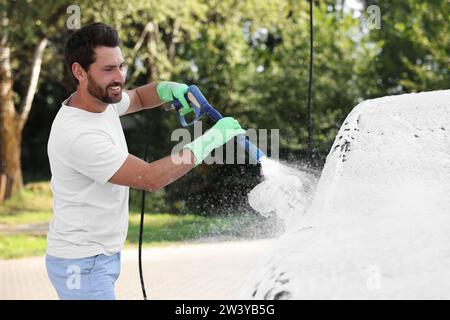 Uomo che copre l'automobile con schiuma all'autolavaggio esterno Foto Stock