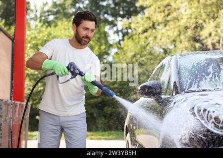 Uomo che copre l'automobile con schiuma all'autolavaggio esterno Foto Stock