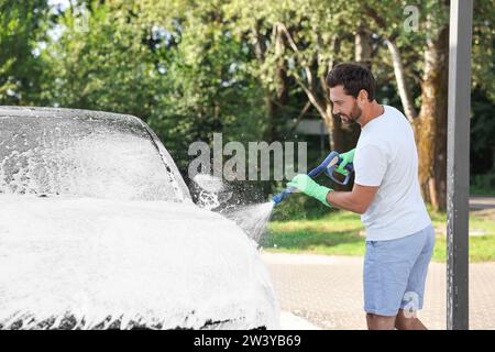 Uomo che copre l'automobile con schiuma all'autolavaggio esterno Foto Stock