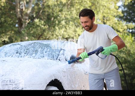 Uomo che copre l'automobile con schiuma all'autolavaggio esterno Foto Stock