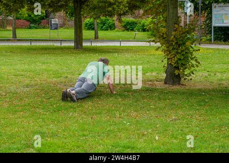 Un uomo anziano sta facendo delle flessioni su un prato nel parco. Foto Stock