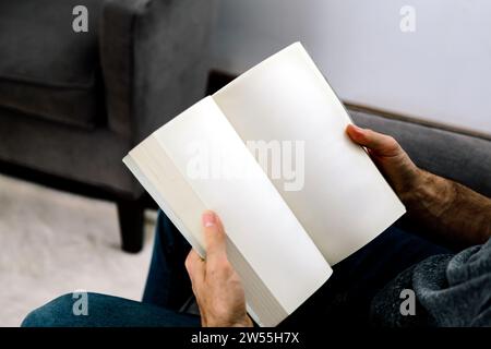 Uomo che legge un libro. Foto ideale di un libro di pagine vuote pronto per il mockup. Un uomo seduto in un soggiorno che tiene in mano un libro aperto. Foto Stock