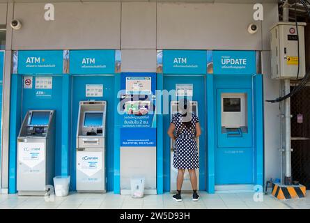 una donna con un abito a pois e un berretto da baseball usa un bancomat a phetchabun, thailandia Foto Stock