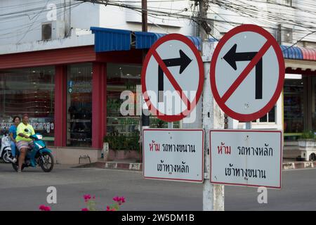 un incrocio stradale in thailandia con segnali stradali che indicano che non vi sono svolte a sinistra e a destra, con conferma scritta, mentre un motociclista e un passeggero guardano Foto Stock