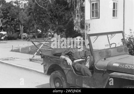 Sergente maggiore polizia militare KNIL posa in jeep. Sul parabrezza, le targhette segnaletiche. Dietro di lui sono visibili dei blocchi stradali mobili, che indicano una caserma come luogo CA. 1947 Foto Stock