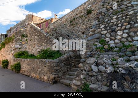 Una scala in pietra che sale su un muro di pietra con edifici in cima. C'è molta vegetazione sul muro e le scale e le pietre sono in parte realizzate Foto Stock