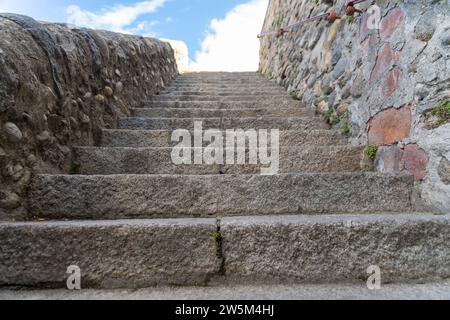 Una scala in pietra che conduce verso l'alto, fiancheggiata da un alto muro in pietra a destra e da una parete piatta a sinistra. In cima si può vedere un cielo blu con le nuvole Foto Stock