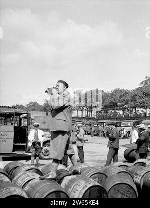 Willem van de poll fotografa a Copenaghen in piedi su botti di vino con auto e piloti in uniforme sullo sfondo, ca. 1934 Foto Stock