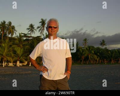 Ritratto di un uomo sorridente che indossa occhiali da sole in piedi su una spiaggia sulla costa occidentale della Costa Rica Foto Stock