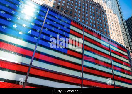 Una vibrante visualizzazione digitale della bandiera americana su un grande schermo tra alti edifici di Times Square New York sotto un cielo blu. Foto Stock